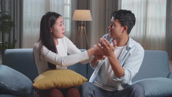 Young Asian Couple Is Watching Tv At Home. Man Switches Channels, Woman Selects Control