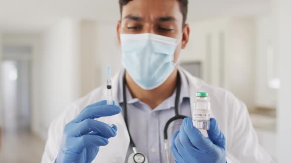 Hispanic male doctor preparing injection wearing face mask