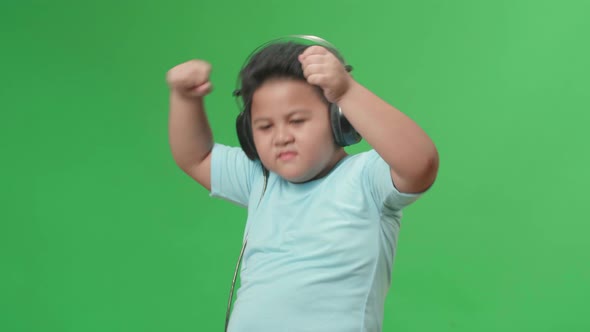 Side View Of Asian Little Boy Listening To Music With Headphones And Dancing In The Green Screen