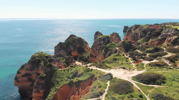 Marked tracks through green vegetation next to Lagos coastline cliffs, Algarve, Portugal