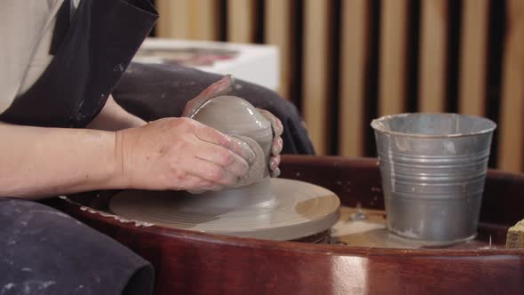 Hands of Elderly Woman Pulls Up a Piece of Wet Clay on the Pottery Wheel Using a Sponge