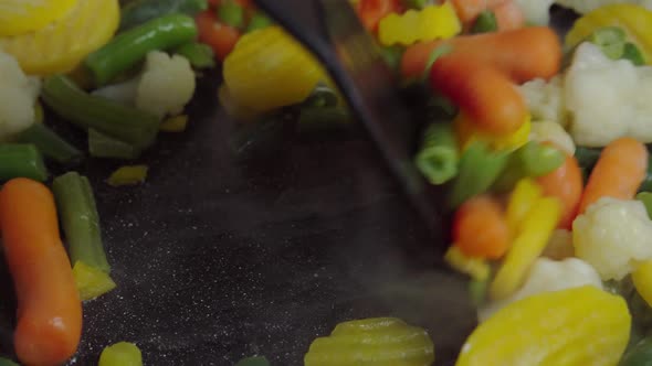 Close up view of steaming frying pan and mixed frozen vegetables. Vegetarian