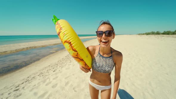 Cheerful Beautiful Young Millennial Woman on Empty Sunny Sandy Beach Holding Yellow Inflatable