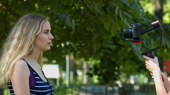 The influencer woman recording her program at park, using stabilizer and mirrorless camera.