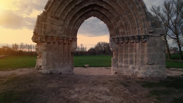 Drone Flying Through a Medieval Arch to Reveal a Scenic Meadow Landscape at Dusk in Sasamon Castile