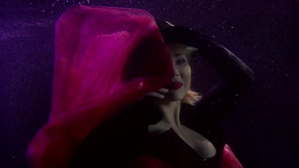Sexy Woman with Red Lips Is Floating Underwater, Dressed in Hat and Gown