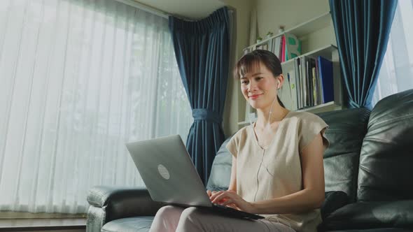 Asian business woman put on earphone, work from home due to Covid-19 typing on notebook computer.