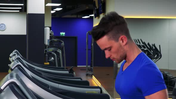 A Young Fit Man Jogs on a Treadmill in a Gym - Closeup From Side