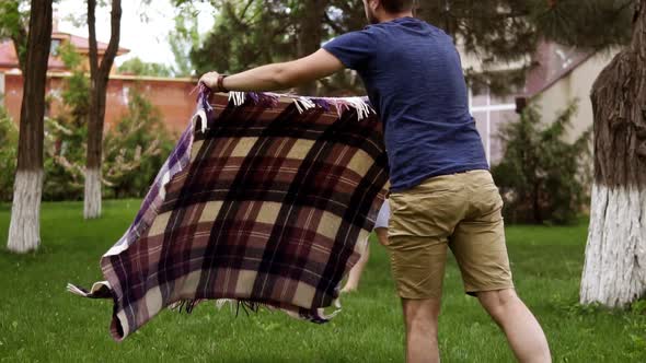 Father in Brown Shorts and Blue Shirt is Spreading the Plaid for Picnic