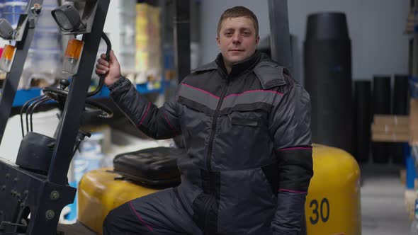 Portrait of Smiling Confident Caucasian Man Standing at Forklift in Warehouse Looking at Camera