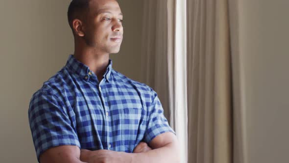 Thoughtful biracial man standing at window and looking into distance