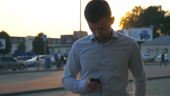 Close Up of Young Successful Businessman in Shirt Standing at Urban Environment and Using Smartphone