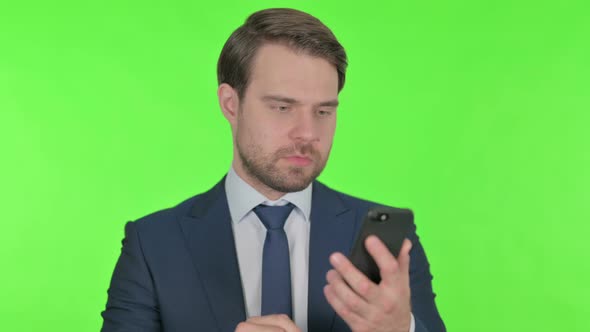 Young Businessman Loss on Smartphone on Green Background