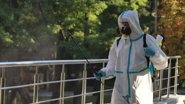 Man in a White Protective Suit Disinfects Handrails and Railings in a Public Area on a Deserted