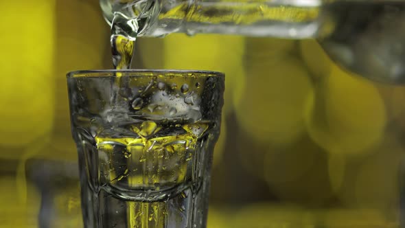 Barman Pour Frozen Vodka From Bottle Into Shot Glass Against Shiny Gold Party Background. Close Up