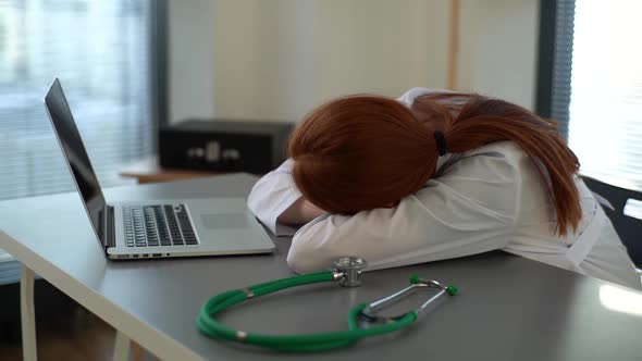 Closeup of Tired Overworked Redhead Female Doctor in White Coat Sleeping at Desk with Laptop and