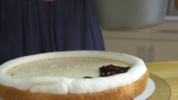 Close up of woman hands making sweet cherry cake with white cream and biscuit.