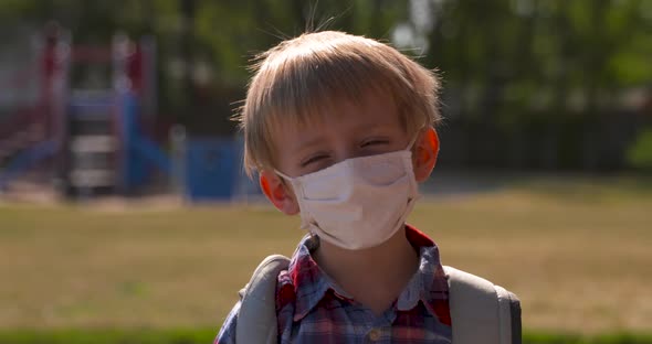 Portrait of a little boy wearing a face mask in a school yard.