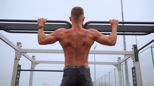 Athletic Man Pumps Up Muscles Doing PullUps Open Sports Ground with Bare Torso