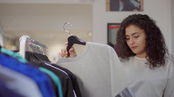 Pretty Woman Is Looking on Sweatshirts in Clothing Store Taking Hangers