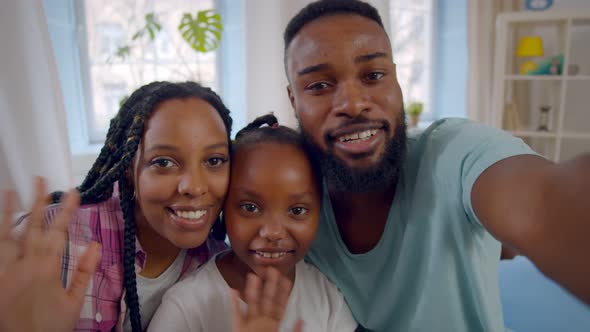 Young Smiling African Parents with Cute Daughter Waving Hands Having Video Conference at Home