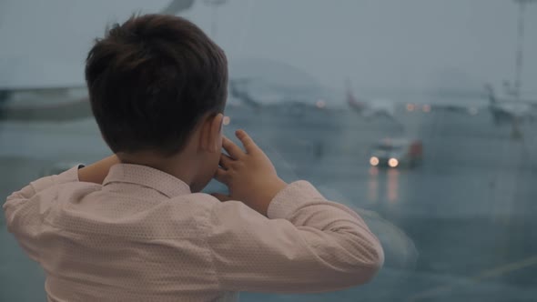 Boy waiting for the flight and looking at airplanes outside