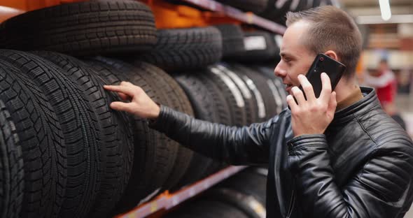 Man Chooses Winter Car Tires in Auto Shop Consulting By Smartphone