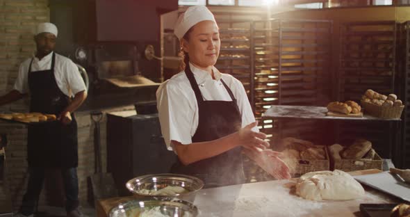 Animation of happy asian female baker clapping hands to clean flour