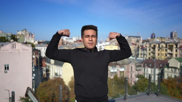 Medium Shot Portrait of Confident Middle Eastern Man Gesturing Strength Standing on Rooftop with
