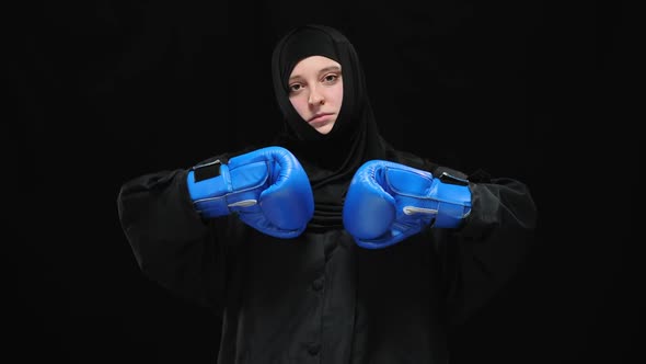 Young Confident Woman in Hijab Bumping Fists in Blue Boxing Gloves Looking at Camera with Serious