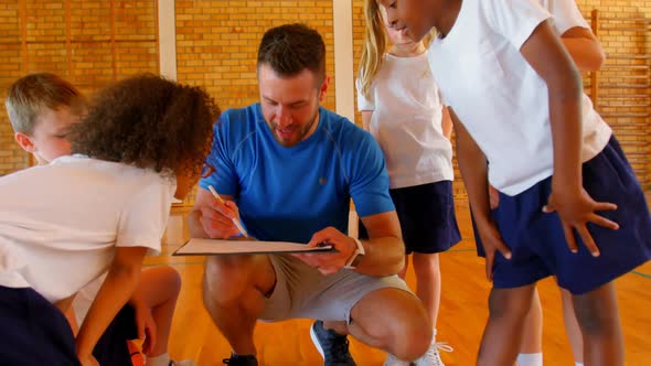 Sports teacher and schoolkids discussing over clipboard in the basketball court 4k