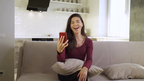 Happy Young Asian Woman Smiles While Using Her Smartphone