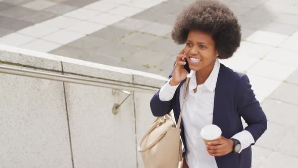 African american businesswoman holding takeaway coffee and talking on smartphone