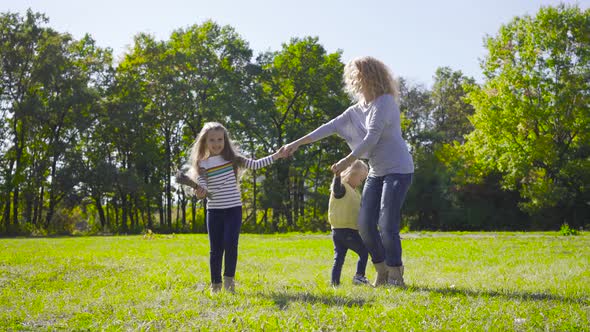 Blond Caucasian Woman with Curly Hair Dancing with Two Pretty Little Girls on the Meadow