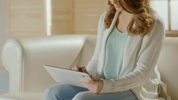 Young Lady Sitting on Couch and Choosing New Dress on Tablet, Online Shopping