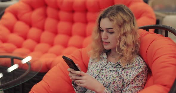 Woman Using Smartphone Sitting on Orange Sofa