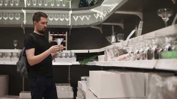 Bearded Man is Looking on Two Glasses for Spirit Drinks in a Tableware Shop