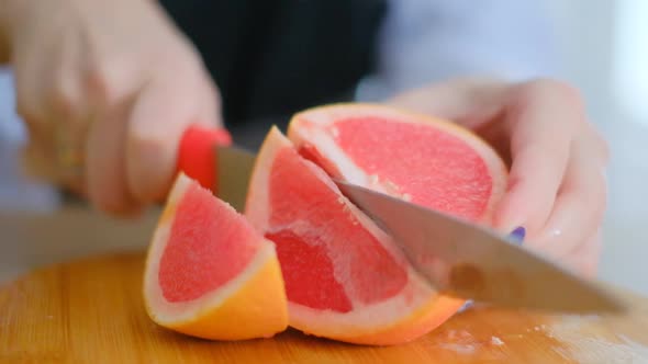 Detail of Female Hands Are Holding a Kitchen Knife and Cutting Grapefruit on a Cutting Board