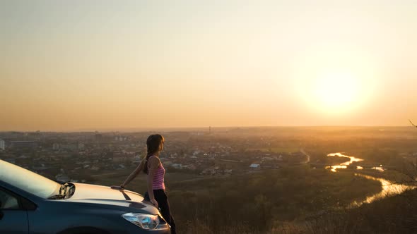 Young Woman Standing Near Her Car Enjoying Warm Sunset View