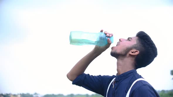 Teenager boy drinks water from bottle in summer outdoor