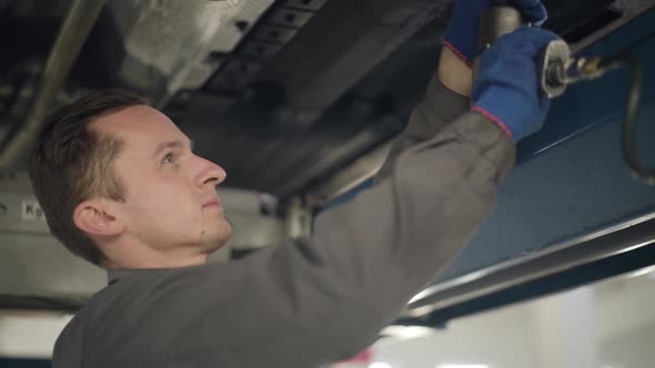 Close-up Side View of Confident Caucasian Man in Workwear Using Professional Equipment for Car