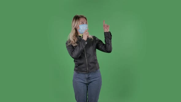 Portrait of Beautiful Young Woman in Medical Protective Face Mask Looking at Camera and Pointing