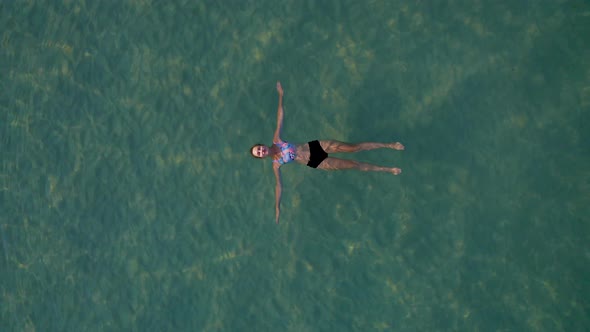 Top View of Young Pretty Sexy Wpman in Black Swimsuit Floating on Water Surface in Crystal Clear