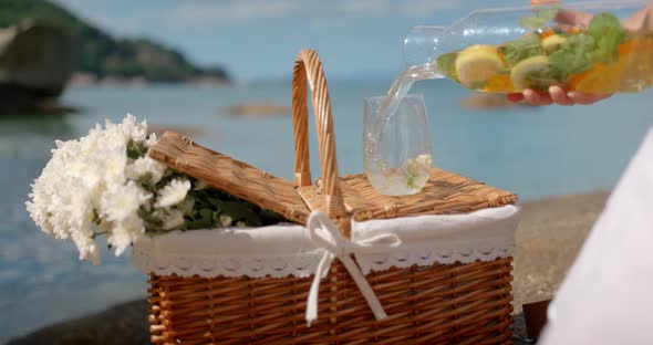 Fresh Lemonade with Mint is Poured Into Glass Standing on the Picnic Basket on Seashore at Daylight