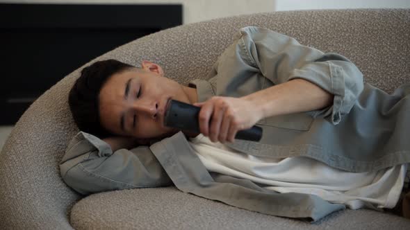 Bored Asian Man Changes TV Channels with Remote Control