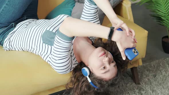 Curly Haired Young Woman on the Couch Listening Music with Headphones