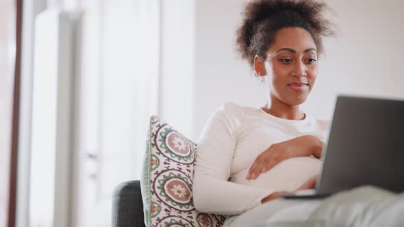 Smiling African pregnant woman watching something on laptop