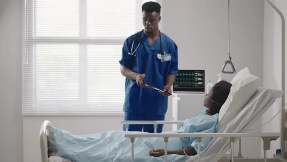 A Male Doctor is Talking to a Patient Lying on a Hospital Bed in a Hospital Ward