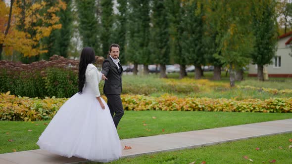 Romantic Couple in Wedding Day Walking Together in Park with Golden Trees