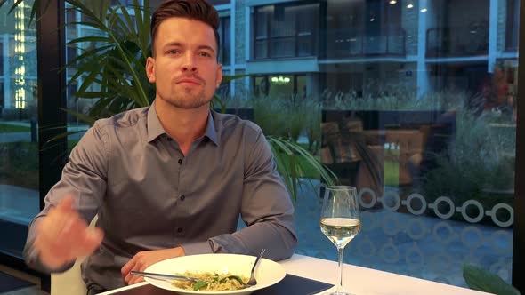 A Young, Handsome Man Sits at a Table in a Restaurant and Calls a Waiter